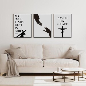 Könnte beinhalten: Drei gerahmte Kunstdrucke mit schwarzem Text und Illustrationen. Die Drucke zeigen religiöse Themen, darunter ein Kreuz und ausgestreckte Hände. Die Drucke werden über einem beigen Sofa in einem Wohnzimmer präsentiert.
