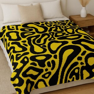 Peut inclure: Une couverture au crochet pixel jaune et noire avec un motif abstrait audacieux. La couverture est présentée sur un lit avec des oreillers blancs et une table de chevet en bois. Le texte en haut indique "PATRON COUVERTURE PIXEL CROCHET • PDF À TÉLÉCHARGER".