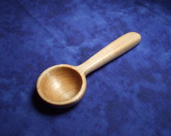 May include: A wooden scoop with a rounded bowl and a long handle. The scoop is made of light-colored wood and is sitting on a blue surface.
