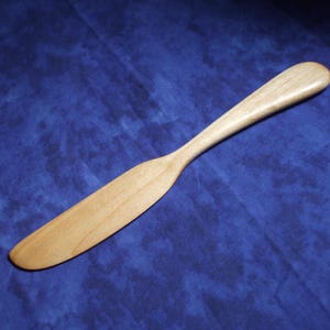May include: A wooden butter knife with a natural finish. The knife is smooth and has a rounded handle.