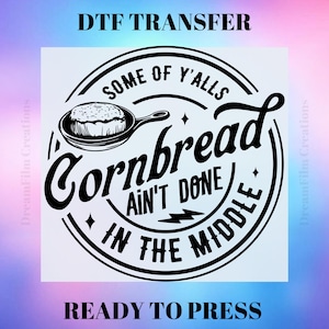 May include: Black and white graphic design with the text "Some of y'alls cornbread ain't done in the middle."  A round, black and white illustration of a piece of cornbread in a skillet is above the text.  The text "DTF Transfer" is at the top of the image and "Ready to Press" is at the bottom.