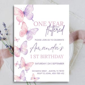 May include: A rectangular birthday invitation card featuring watercolor butterflies in shades of pink and purple on a white background. The text reads: ONE YEAR FLUTTERED, PLEASE JOIN US TO CELEBRATE, Amanda's 1 ST BIRTHDAY, SATURDAY | 24 | SEPTEMBER, 123 MAPLE SREET, AUSTIN, TX 78701, RSVP TO JOHN, 459-789-412.