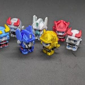 Op de afbeelding: Zeven kleine, kleurrijke, 3D-geprinte robotfiguren. De robots staan in verschillende poses en hebben verschillende gekleurde details, waaronder rood, blauw, geel, wit en grijs.