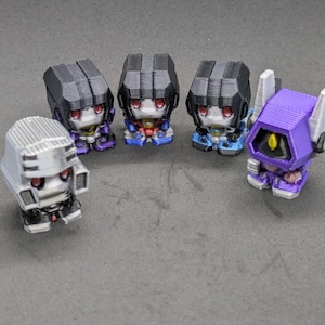 May include: Five small, 3D printed figurines of robots. The robots are in various poses and have different colored details. The robots are all about 2 inches tall.