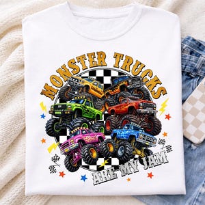 Op de afbeelding: Wit T-shirt met een kleurrijke afbeelding van monstertrucks in geel, groen, roze en blauw. De tekst "MONSTER TRUCKS ARE MY JAM" is in een cirkel rond de trucks gedrukt.