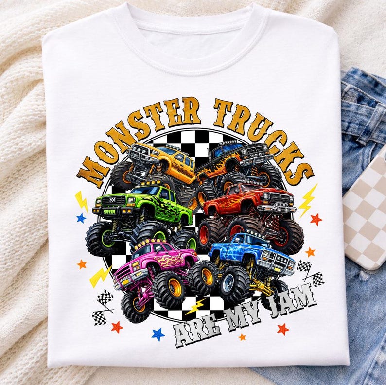 Op de afbeelding: Wit T-shirt met een kleurrijke afbeelding van monstertrucks in geel, groen, roze en blauw. De tekst "MONSTER TRUCKS ARE MY JAM" is in een cirkel rond de trucks gedrukt.