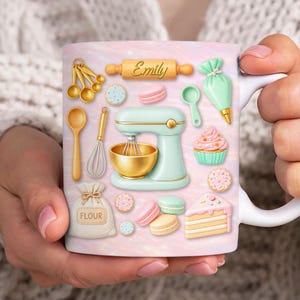 May include: A white ceramic mug with a pastel pink design, decorated with baking-related illustrations. The design includes a stand mixer, measuring spoons, rolling pin with the name "Emily", macarons, and a cupcake. The mug is held by a person.
