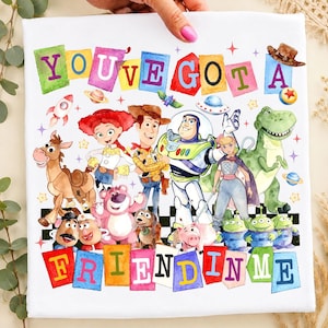 Può includere: Tela bianca con un'illustrazione colorata dei personaggi di Toy Story. La frase "YOU'VE GOT A FRIEND IN ME" è scritta in lettere colorate. L'immagine include Woody, Buzz Lightyear e altri personaggi del film d'animazione.