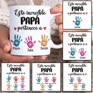 May include: White ceramic mug with the text "Este increible PAPÁ pertenece a" and three colorful handprints. The names "Mark", "Julia", and "Sarah" are below the handprints. Additional designs with handprints and text are also shown.