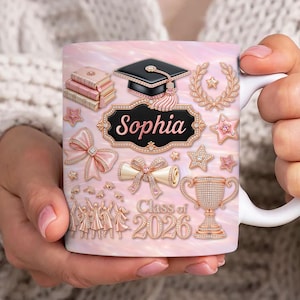 Op de afbeelding: Witte keramische mok met een roze achtergrond, versierd met afstudeer-thema graphics. Voorzien van een afstudeerhoed, sterren, een diploma en de naam "Sophia" in elegant schrift. De mok bevat ook de tekst "Class of 2026".