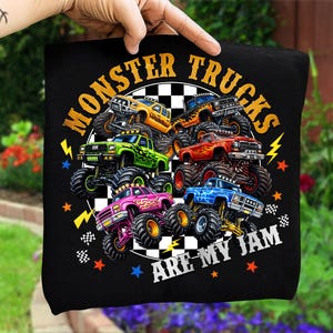 Op de afbeelding: Zwart T-shirt met een kleurrijke afbeelding van monstertrucks. Het ontwerp toont monstertrucks in geel, groen, rood, roze en blauw, met de tekst "MONSTER TRUCKS ARE MY JAM" in een cirkelvorm.