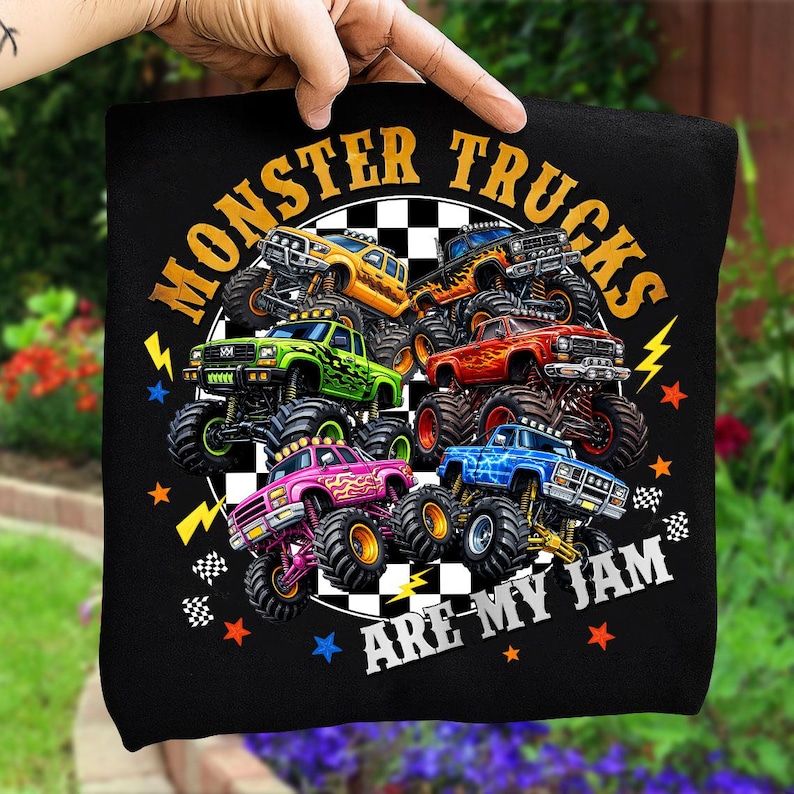 Op de afbeelding: Zwart T-shirt met een kleurrijke afbeelding van monstertrucks. Het ontwerp toont monstertrucks in geel, groen, rood, roze en blauw, met de tekst "MONSTER TRUCKS ARE MY JAM" in een cirkelvorm.