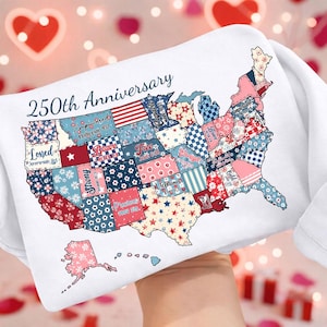 May include: A white pillow with a map of the United States, featuring a patchwork design with various patterns and colors. The pillow is labeled "250th Anniversary" and includes words like "Loved," "Brave," and "Victorious" on the states.