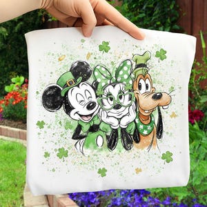 Könnte beinhalten: Weißes Grafikdesign zum St. Patrick's Day mit Micky Maus, Minnie Maus und Goofy. Micky trägt einen grünen Hut, Minnie trägt eine grüne Schleife und Brille, und Goofy trägt einen grünen Hut und Schal. Grüne Kleeblätter und Goldmünzen sind verstreut.