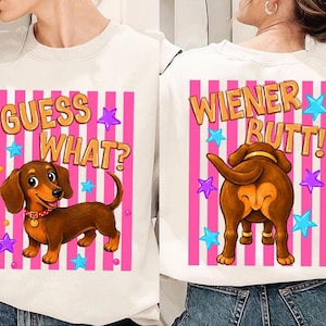 Puede incluir: Sudadera blanca con una ilustración de perro salchicha de dibujos animados. La parte delantera presenta el texto "GUESS WHAT?" y el perro. La parte trasera muestra el trasero del perro con el texto "WIENER BUTT!" y estrellas.