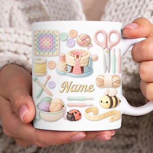 Könnte beinhalten: Weiße Keramiktasse mit verschiedenen Handarbeits-Elementen, darunter Garn, Knöpfe, Schere und eine Strickmaschine. Die Tasse zeigt das Wort "Name" in einer Schreibschrift und eine Cartoon-Biene.
