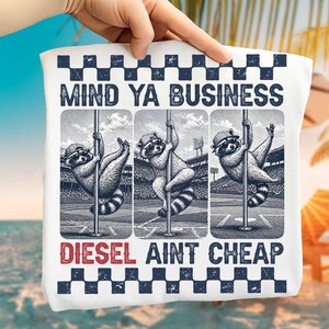 May include: White tote bag with a design of three raccoons on poles, set against a stadium background. The text "MIND YA BUSINESS" and "DIESEL AINT CHEAP" are printed above and below the raccoons in a bold font, with a checkered border.