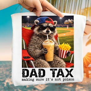 May include: White tote bag with a raccoon wearing sunglasses and a baseball cap, holding a drink and fries. The text "DAD TAX" and "making sure it's not poison" are printed below the image. The raccoon is sitting in a red chair.