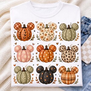 May include: A white t-shirt featuring a grid of nine pumpkin illustrations, each with mouse-ear-shaped stems. The pumpkins display various patterns including plaid, floral, polka dot, and leopard print in orange, green, black, and pink tones.
