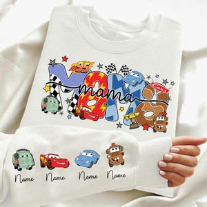 May include: White sweatshirt with a colourful graphic design featuring the word "Mama" in a playful font, along with car illustrations and the number "95". The sleeves have car illustrations with the word "Name" below each.