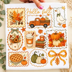 May include: A white fabric square featuring a colourful autumn-themed print with the text Hello fall. Illustrations include a pumpkin-filled truck, a goose with a green bow, a floral pitcher, a coffee cup, stacked books, a pie, and pumpkins.