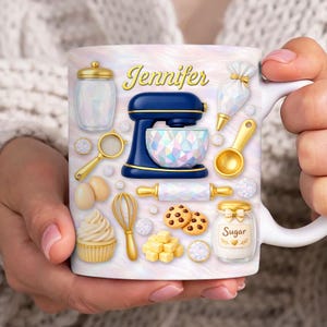 May include: White ceramic mug with baking-themed illustrations. The mug features a blue and gold stand mixer, a jar of sugar, cookies, and the name "Jennifer" in gold script. Other baking tools are also featured.