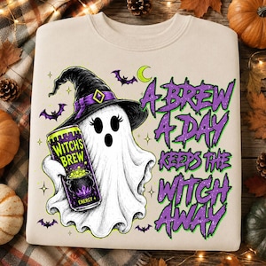 May include: A beige crewneck sweatshirt featuring a graphic of a white ghost wearing a black witch hat and holding a purple energy drink can labeled Witch's Brew. The text reads A BREW A DAY KEEPS THE WITCH AWAY, surrounded by small bats and stars.