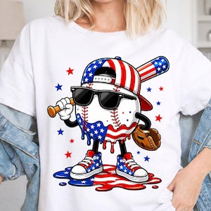 May include: White t-shirt featuring a cartoon baseball character wearing sunglasses, a baseball cap, and sneakers, all in red, white, and blue. The baseball is holding a bat and a baseball glove. Red and blue stars are scattered around the design.
