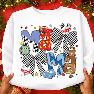May include: White sweatshirt with the word "MAMA" in a playful design featuring race cars and checkered bows. The letters are in blue, red, and brown, with star and flag accents. A fun, themed top for fans of the Cars movie.