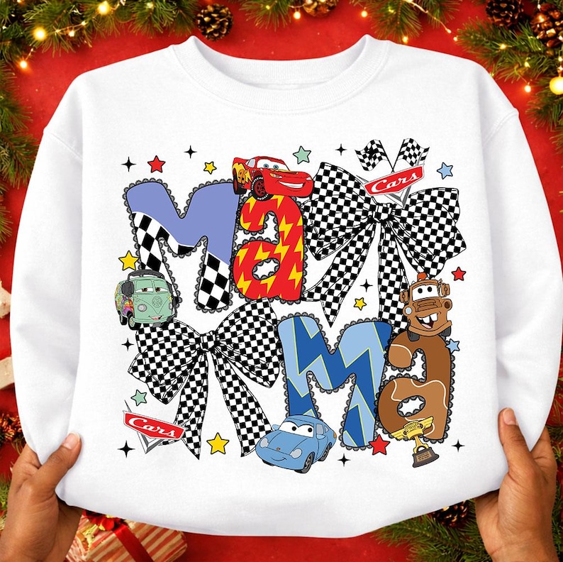 May include: White sweatshirt with the word "MAMA" in a playful design featuring race cars and checkered bows. The letters are in blue, red, and brown, with star and flag accents. A fun, themed top for fans of the Cars movie.