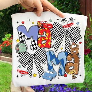 May include: White square pillow with the word "Mama" in blue, red, and brown letters, decorated with cartoon cars and checkered bows. The pillow has a Cars theme with stars and the word "Cars".