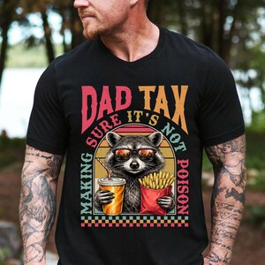 May include: Black t-shirt featuring a raccoon wearing sunglasses, holding a drink and fries. The text reads "DAD TAX, SURE IT'S NOT POISON, MAKING". The design has a retro colour scheme.