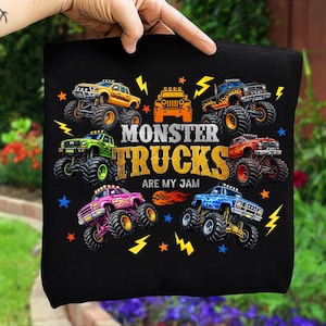 May include: Black t-shirt with a design of colourful monster trucks in yellow, orange, green, pink, and blue. The text "MONSTER TRUCKS ARE MY JAM" is displayed. Lightning bolt and star graphics surround the trucks.