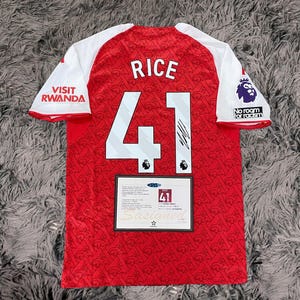 May include: Red and white soccer jersey with the name "RICE" and the number "41" printed on the back. The jersey has white sleeves and the words "VISIT RWANDA" are printed on the left sleeve. The right sleeve has the words "No room for racism".