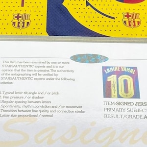 May include: A blue and red soccer jersey with a certificate of authenticity. The jersey has the number 10 and the name "LAMINE YAMAL" printed on it. The certificate states the item is a signed jersey and is authentic.
