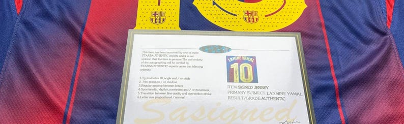 May include: A blue and red soccer jersey with a certificate of authenticity. The jersey has the number 10 and the name "LAMINE YAMAL" printed on it. The certificate states the item is a signed jersey and is authentic.