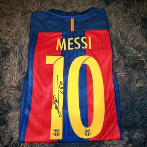 May include: A blue, red, and yellow soccer jersey with the number "10" and the name "MESSI" on the back. The jersey has the FC Barcelona logo on the front and back.