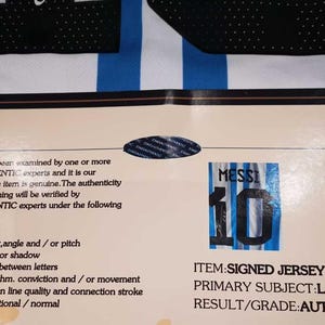 May include: A signed Lionel Messi jersey with the number 10, accompanied by a certificate of authenticity from STARSAUTHENTIC. The jersey features blue and white stripes, with black accents.