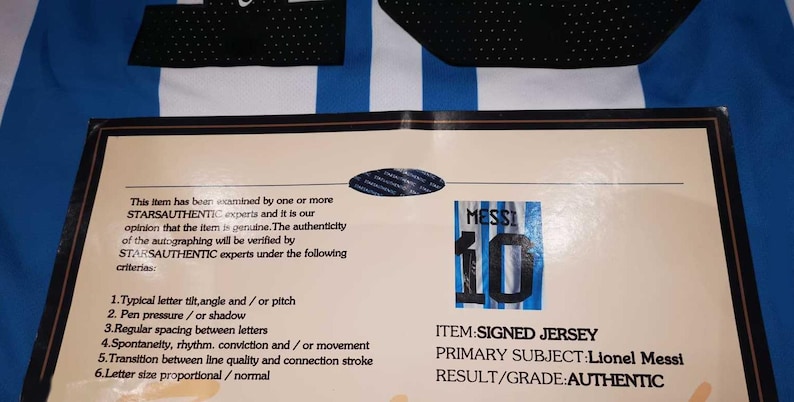 May include: A signed Lionel Messi jersey with the number 10, accompanied by a certificate of authenticity from STARSAUTHENTIC. The jersey features blue and white stripes, with black accents.