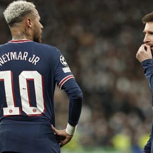 May include: Two soccer players in navy blue jerseys with red and white accents are seen on a field. One jersey displays "NEYMAR JR" and the number "10". The other player is biting his fingernails. The scene is set in a stadium.