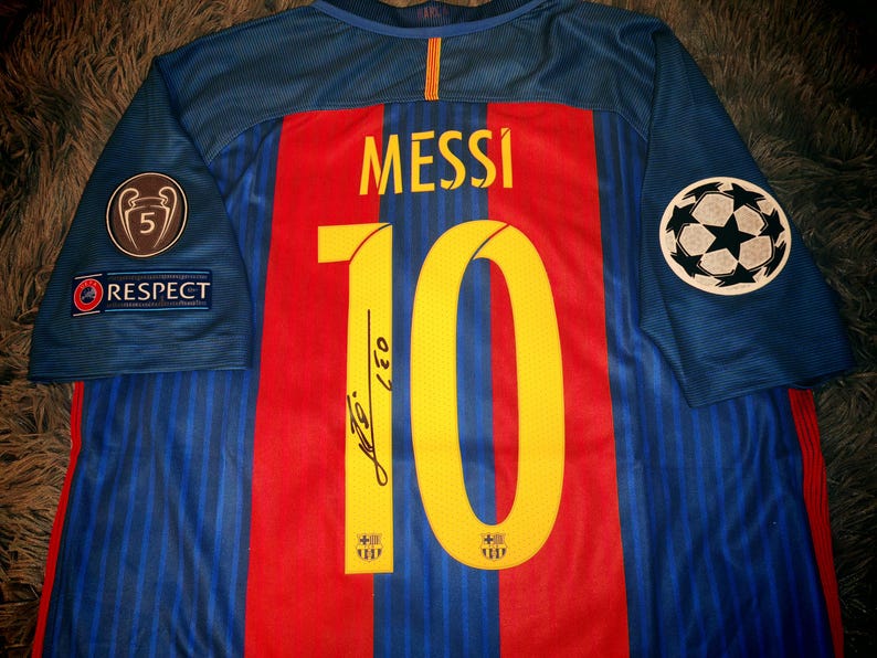 May include: A blue soccer jersey with red and yellow stripes. The number 10 is printed on the back with the name "MESSI" above it. The jersey has a Champions League patch on the right sleeve and a patch that says "RESPECT" on the left sleeve.