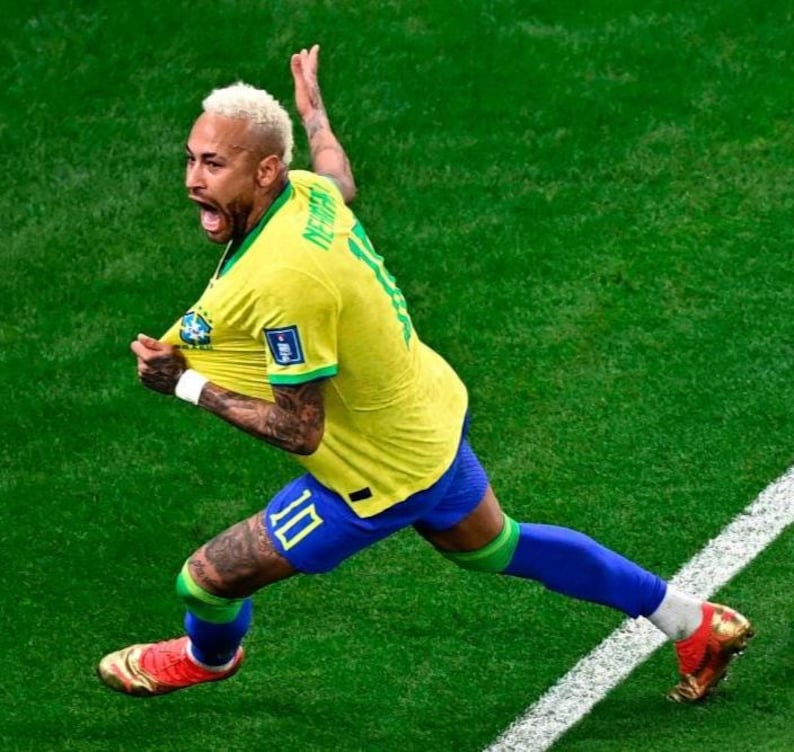 May include: A soccer player wearing a yellow jersey with the name Neymar and the number 10 on the back, paired with blue shorts, green socks, and gold cleats, celebrating on a green field with a white boundary line visible on the grass.
