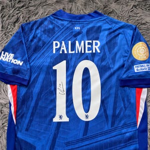 May include: A blue soccer jersey with the name "PALMER" and the number "10" in white. The jersey has a signature below the number and the "Live Nation" logo on the sleeve. The jersey also has the "FIFA" and "Football Unites the World" logos.