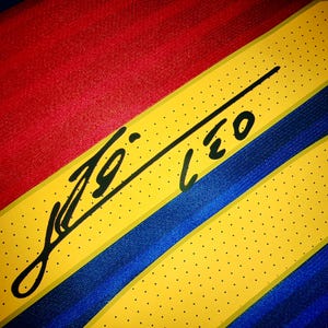 May include: A yellow, blue, and red striped fabric with a black signature that reads "Leo" on it.