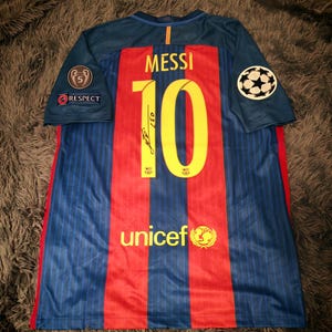 May include: A blue and red soccer jersey with the number 10 and the name "MESSI" on the back. The jersey has a UNICEF logo and a Champions League patch on the sleeve.
