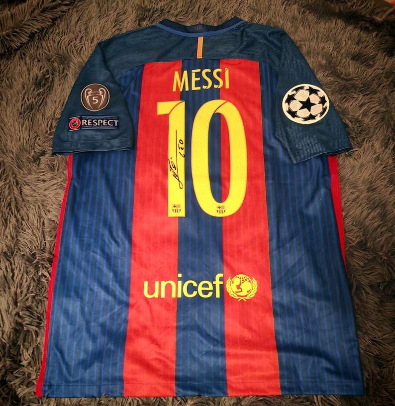 May include: A blue and red soccer jersey with the number 10 and the name "MESSI" on the back. The jersey has a UNICEF logo and a Champions League patch on the sleeve.