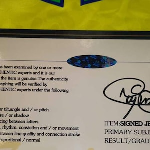 May include: A rectangular certificate of authenticity with a black border on a bright yellow background. The document features the text STARSAUTHENTIC, a holographic seal, a signature, and the text ITEM: SIGNED JERSEY, PRIMARY SUBJECT: NEYMAR JR, RESULT/GRADE: AUTHENTIC.