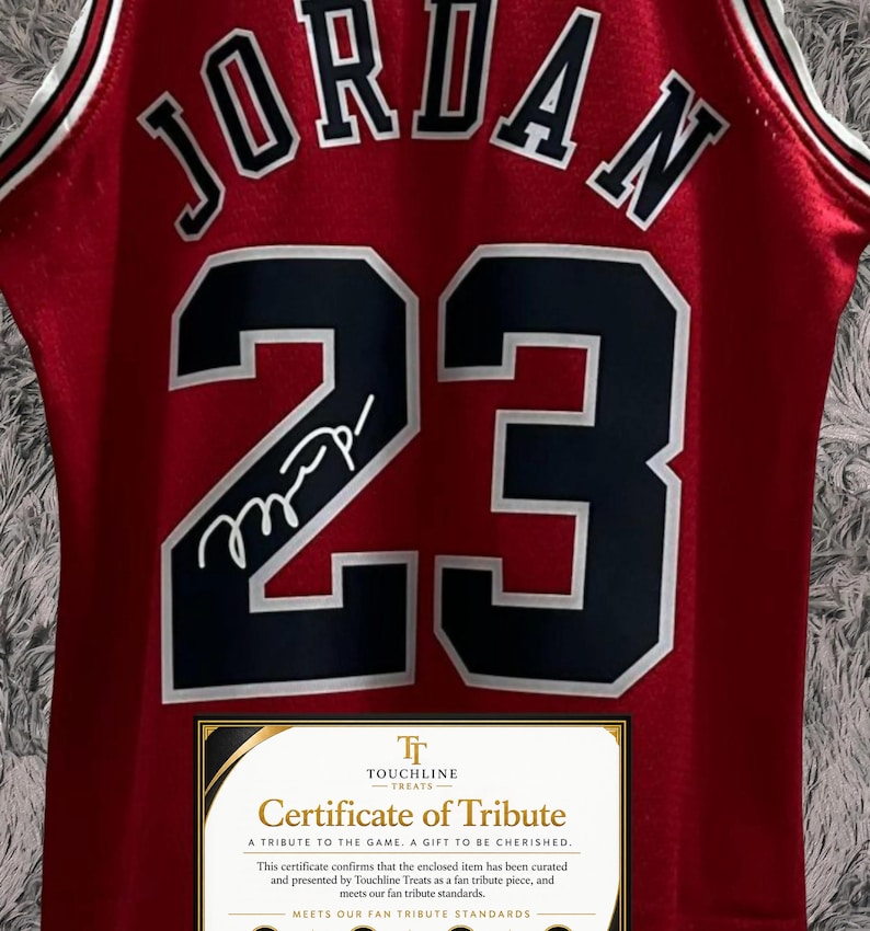 Peut inclure: Un maillot de basket rouge portant le nom JORDAN et le num&eacute;ro 23 en noir avec des contours blancs. Une signature blanche est visible sur le chiffre 2. Un certificat de tribut rectangulaire de Touchline Treats est plac&eacute; en bas.