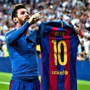 May include: A soccer player in a blue jersey holds up a red and blue soccer jersey with the number 10 and the name "MESSI" on the back. The jersey also has the UNICEF logo and the text "unicef".