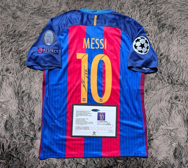 May include: A blue and red soccer jersey with the number 10 and the name "MESSI" on the back. The jersey has a white star and the word "RESPECT" on the left sleeve. The jersey also has a Champions League patch on the right sleeve.